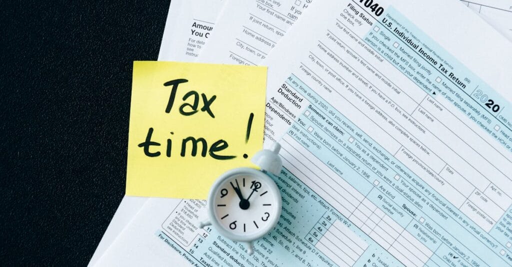 pexels-photo-6863259-6863259 A stack of tax forms with a clock and yellow sticky note saying 'Tax time!' indicating urgency.